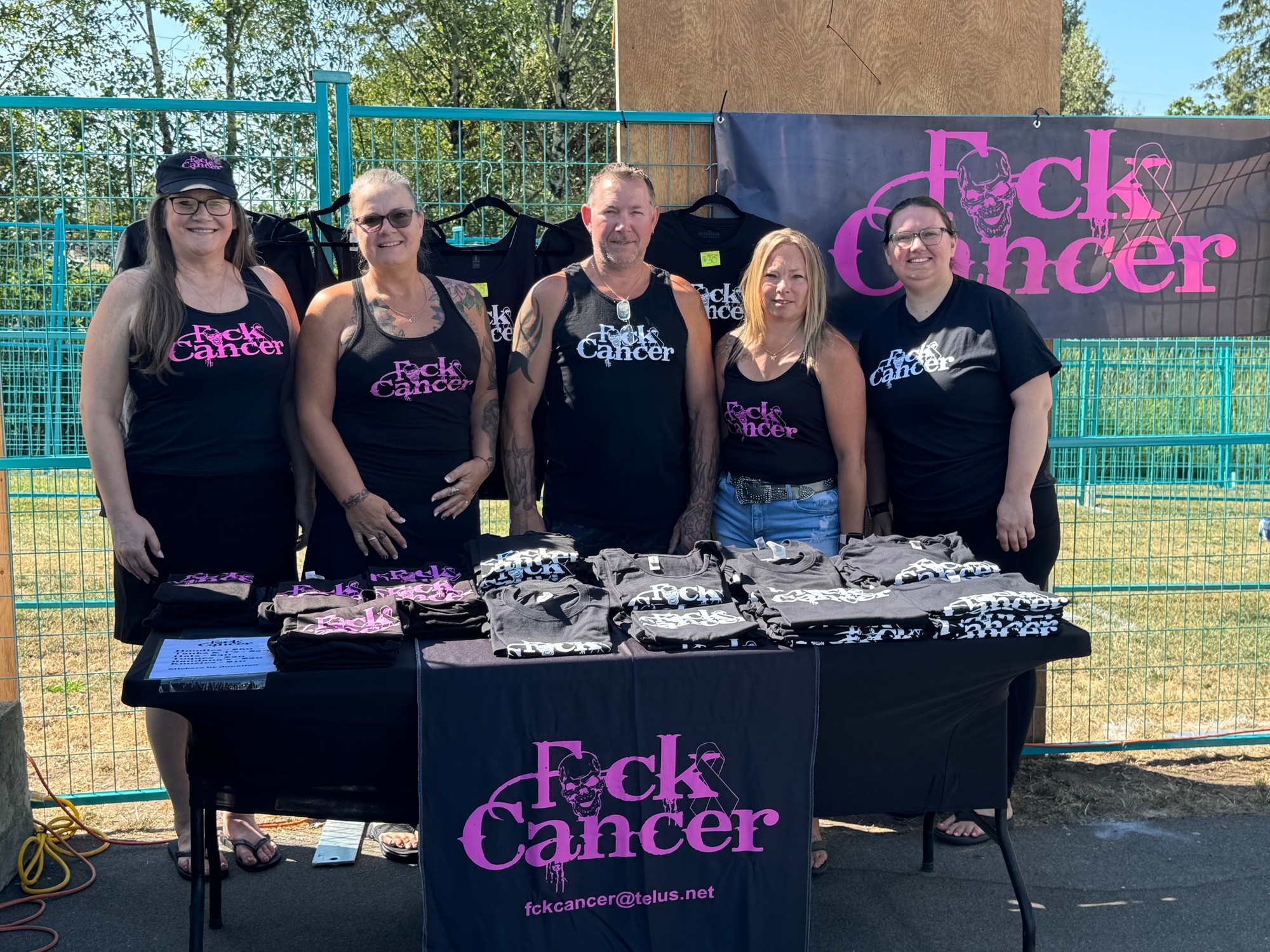 Five volunteers at an FCK Cancer merch table with banner