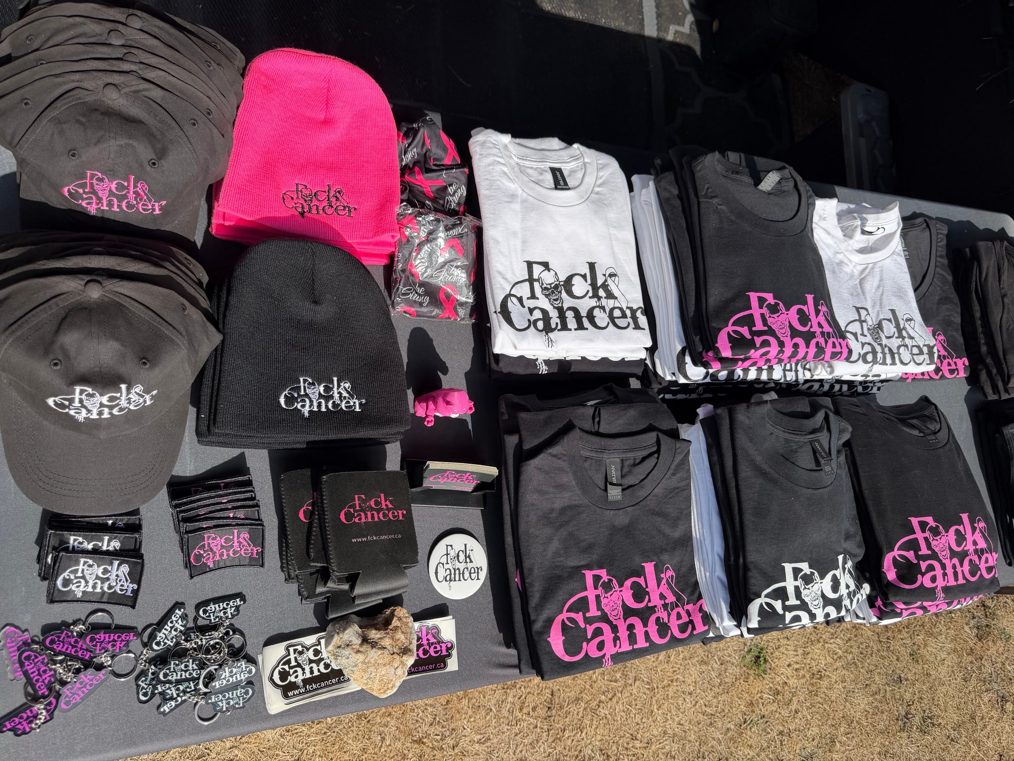 FCK Cancer hats, shirts, koozies and patches laid out on a table